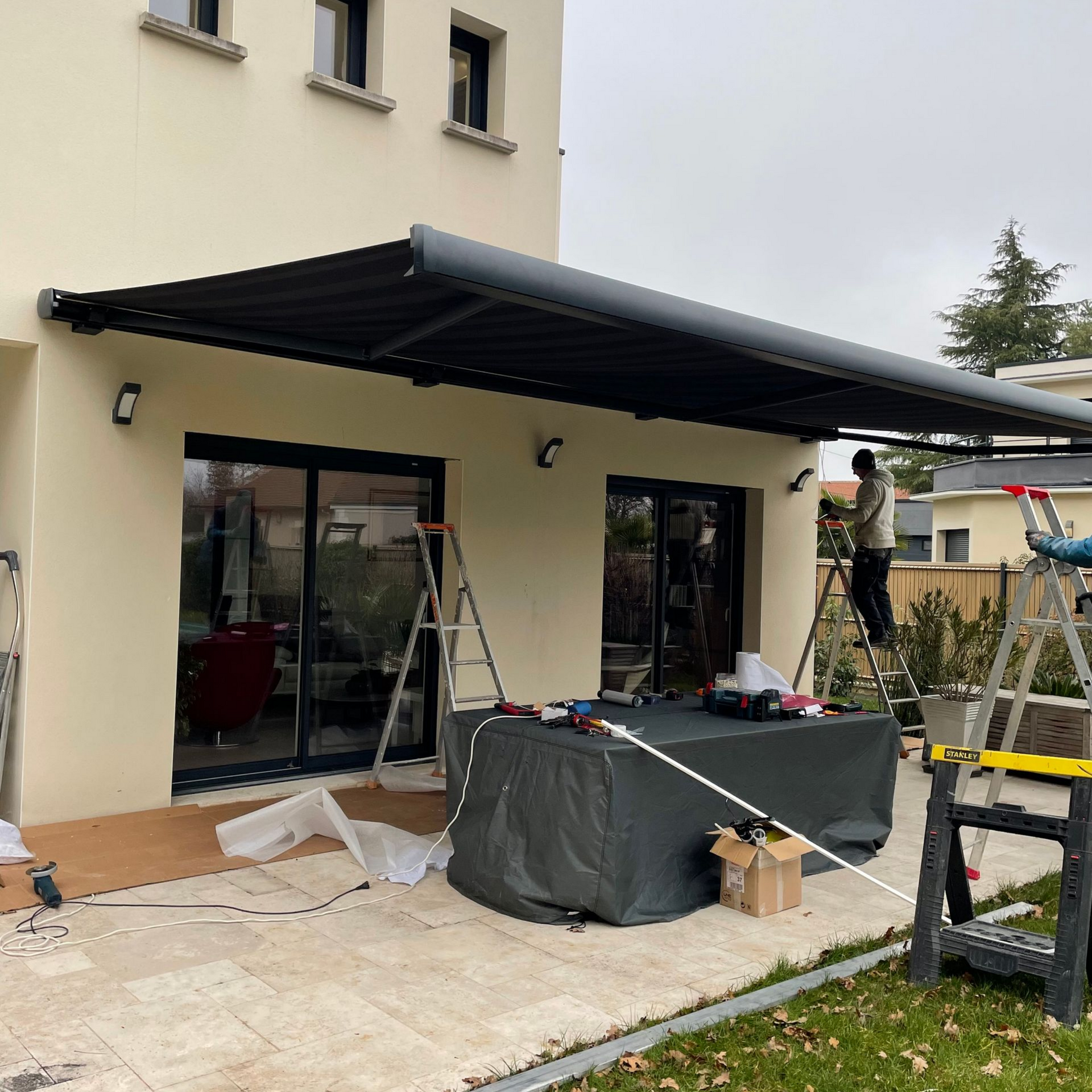 Des ouvriers installent un store à banne au-dessus des portes-fenêtres d'une maison.