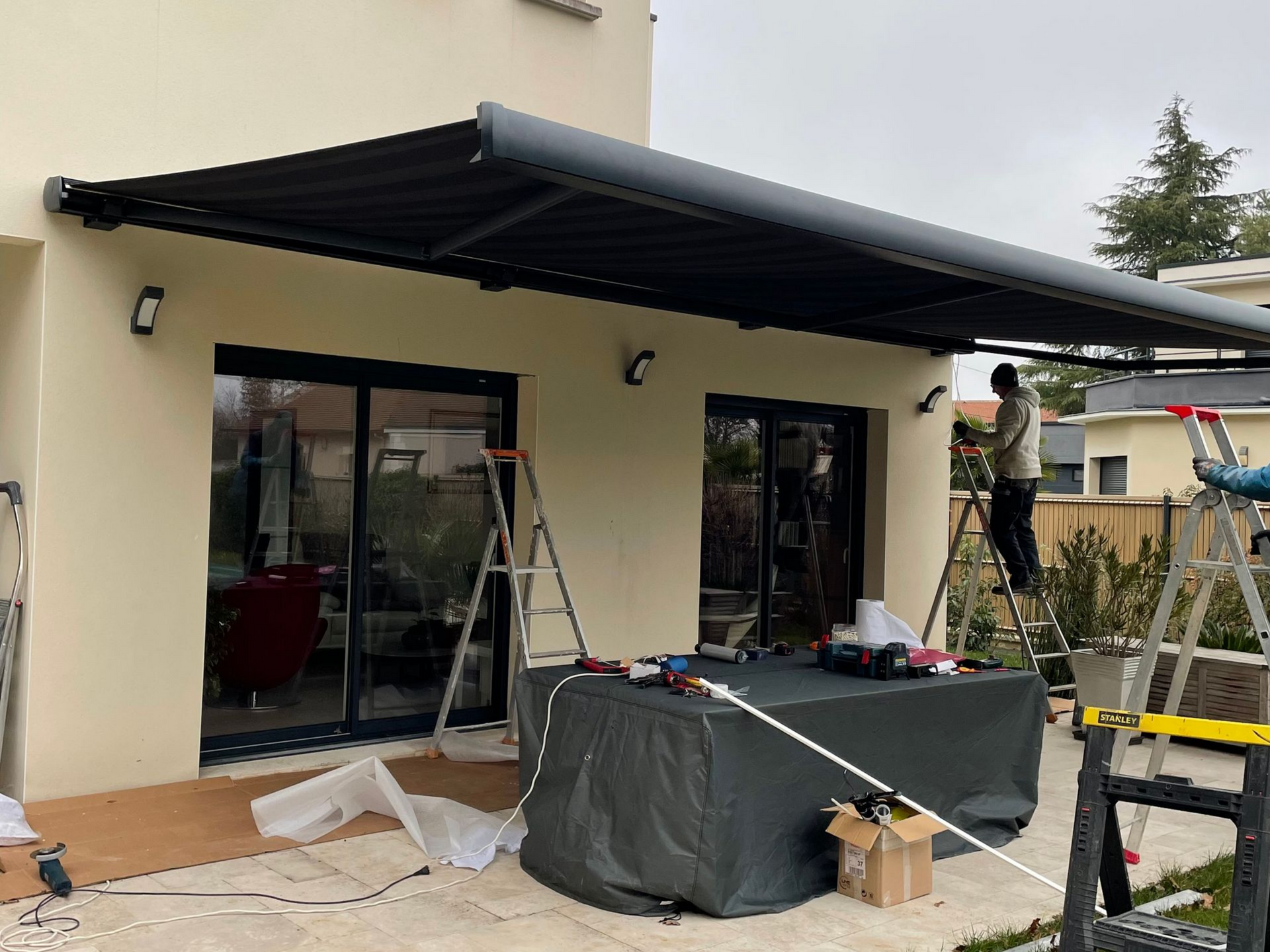 Des ouvriers installent un store à banne au-dessus des portes-fenêtres d'une maison.