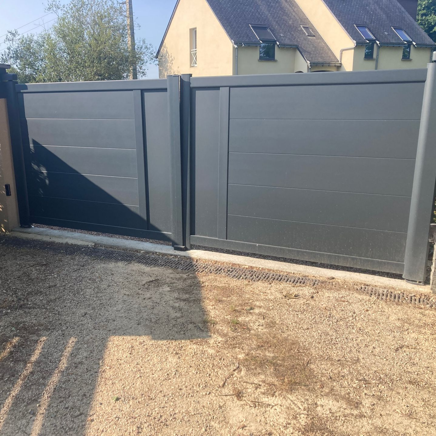 Portail d'allée en métal gris à lattes horizontales.