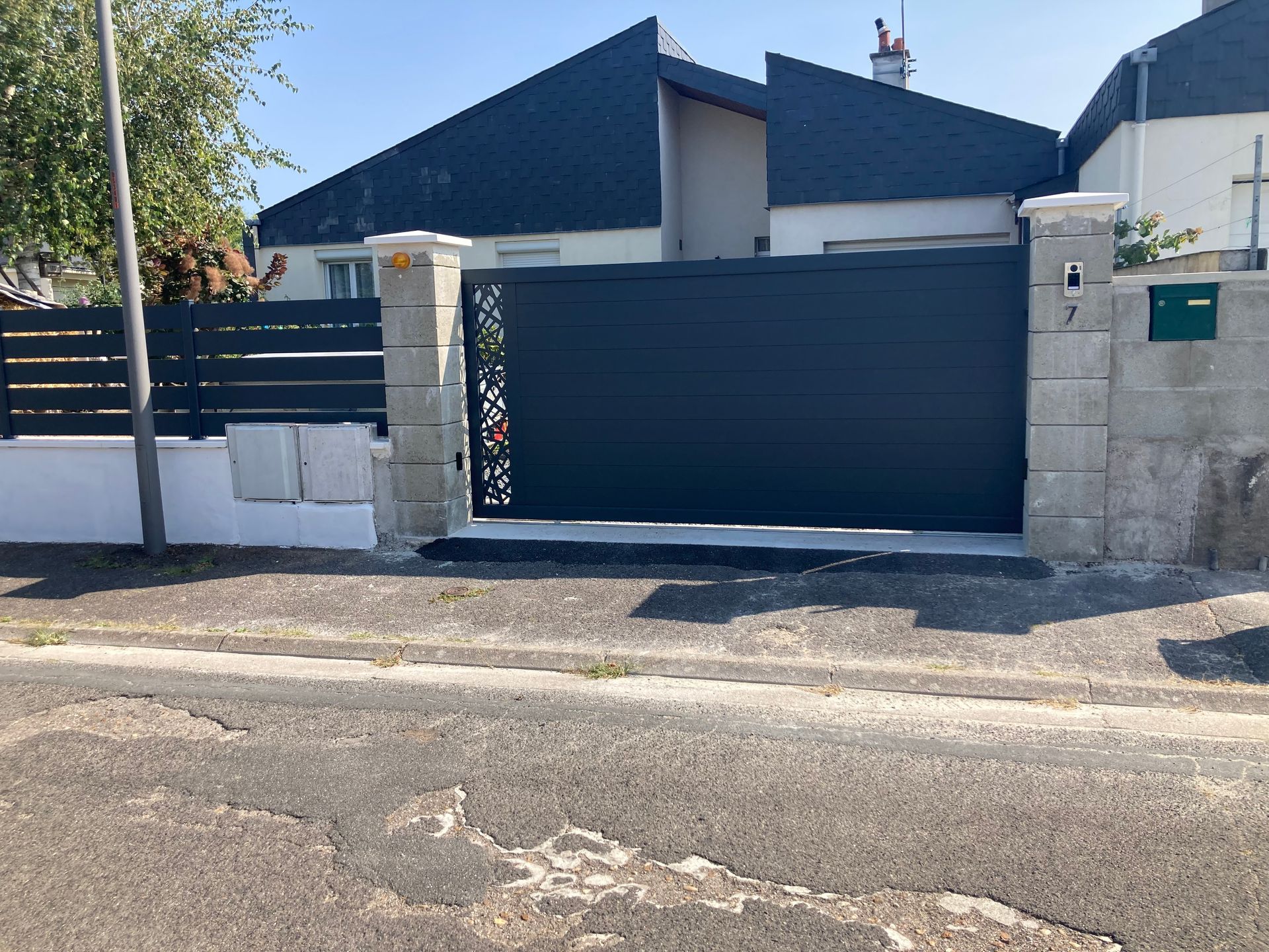 Un portail coulissant gris foncé devant une maison, avec un panneau décoratif sur le côté gauche.