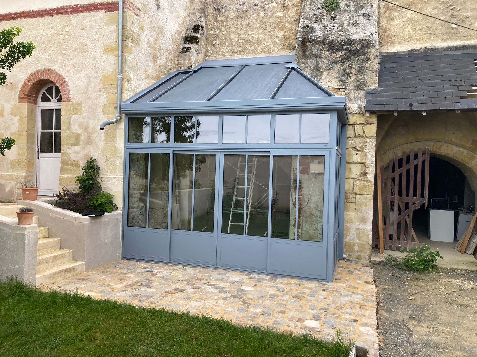 Maison moderne avec store banne de couleur claire au-dessus d'une terrasse bordée par une piscine.