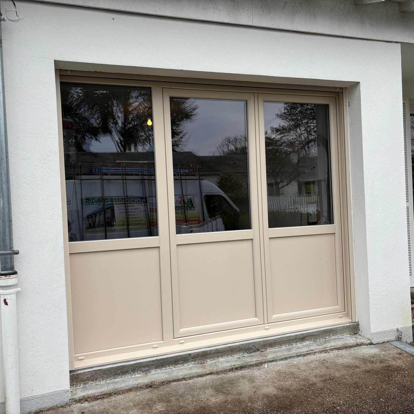 Porte-fenêtre à triple vitrage beige sur une façade blanche.
