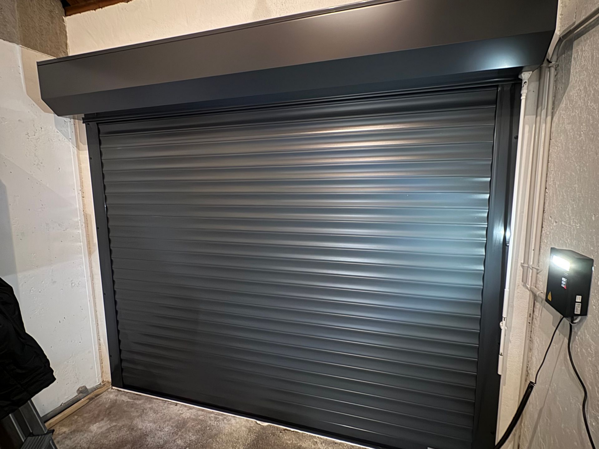 Porte sectionnelle grise fermée dans une niche, avec boîtier de commande à droite.