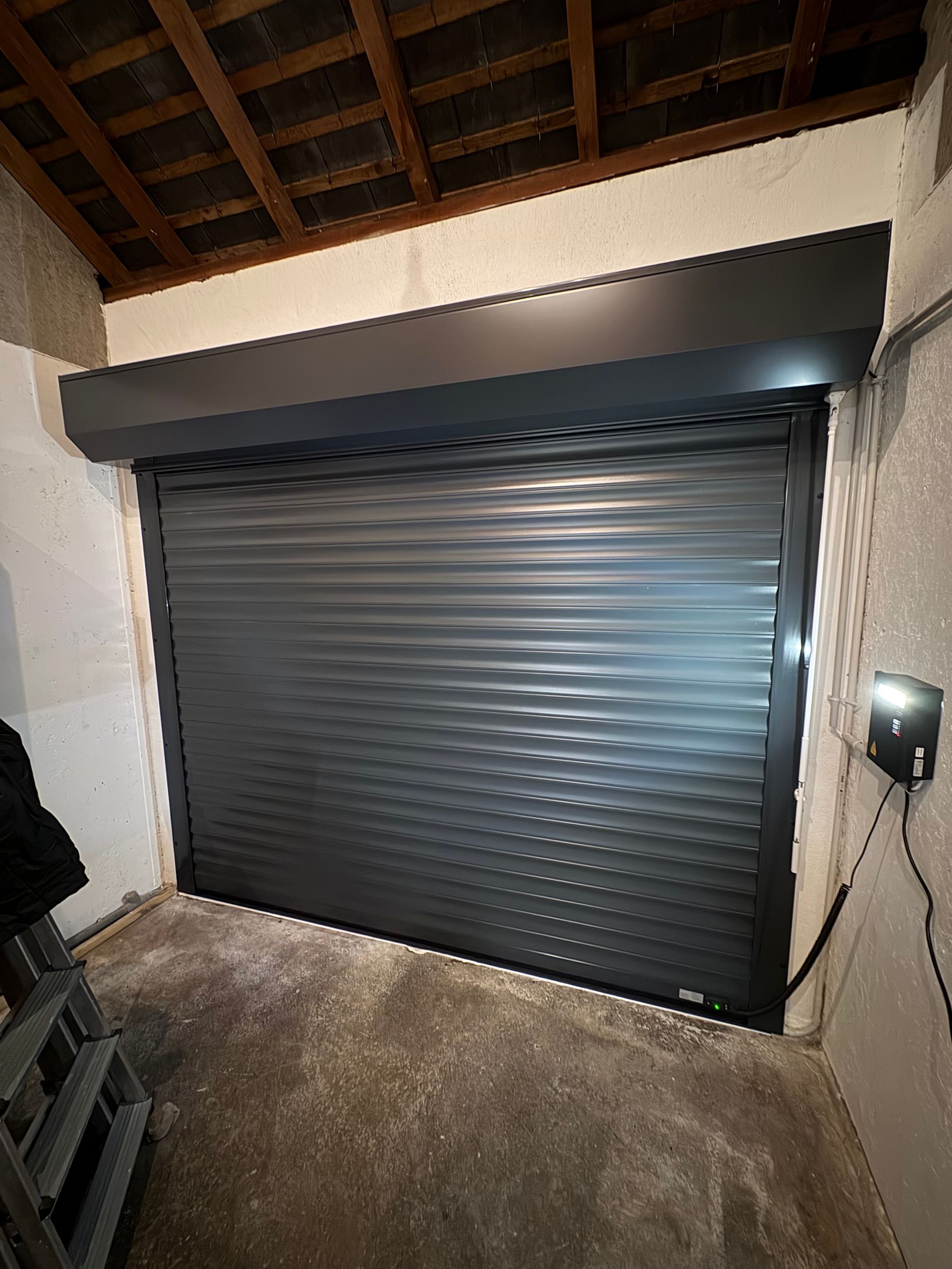 Porte sectionnelle grise fermée dans une niche, avec boîtier de commande à droite.