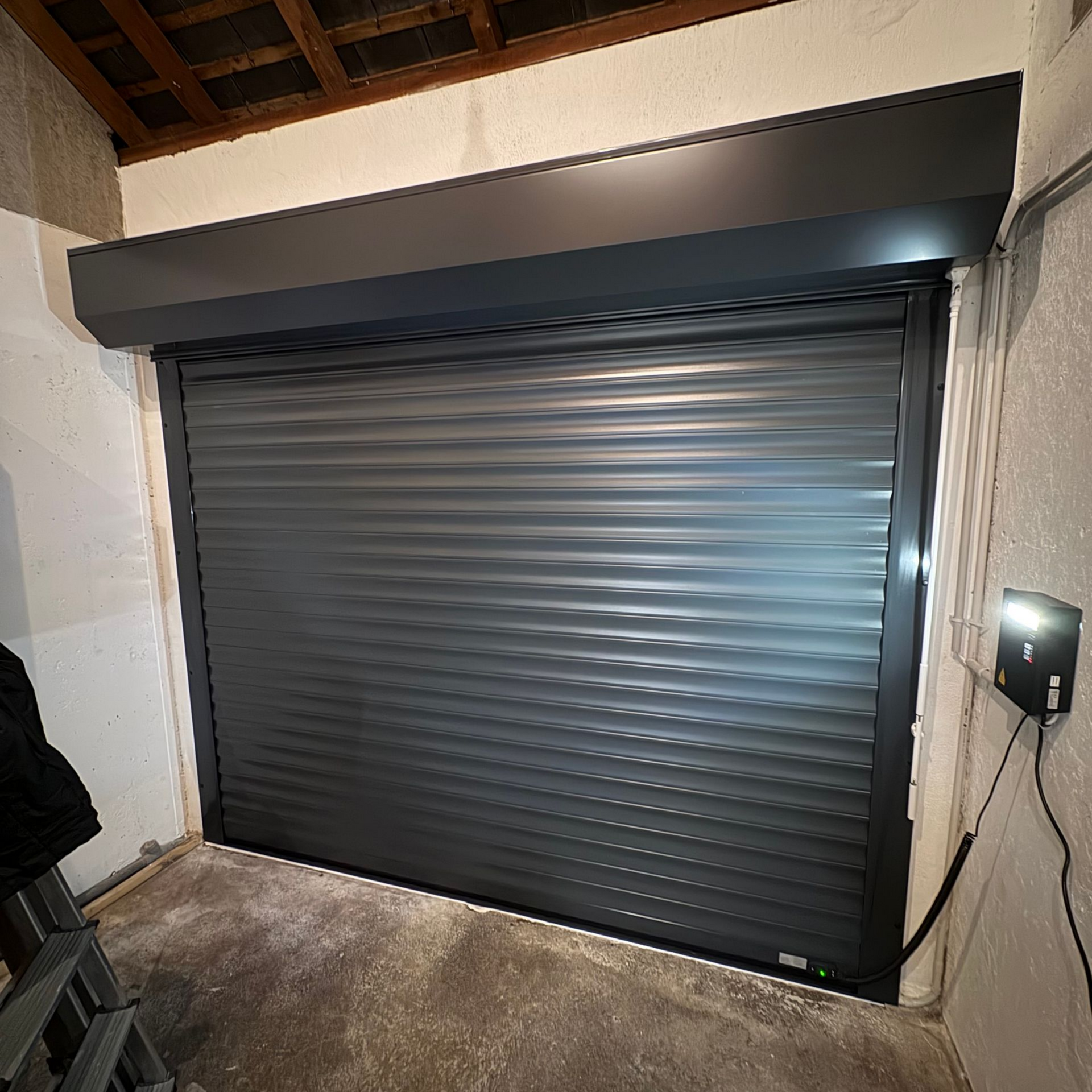 Porte sectionnelle grise fermée dans une niche, avec boîtier de commande à droite.