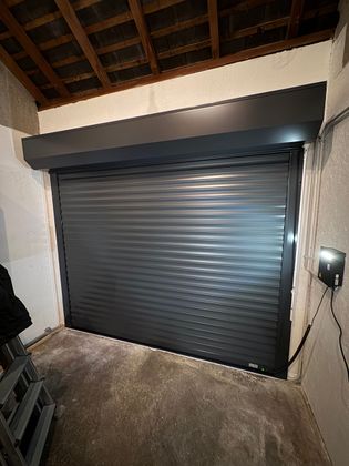 Porte sectionnelle grise fermée dans une niche, avec boîtier de commande à droite.