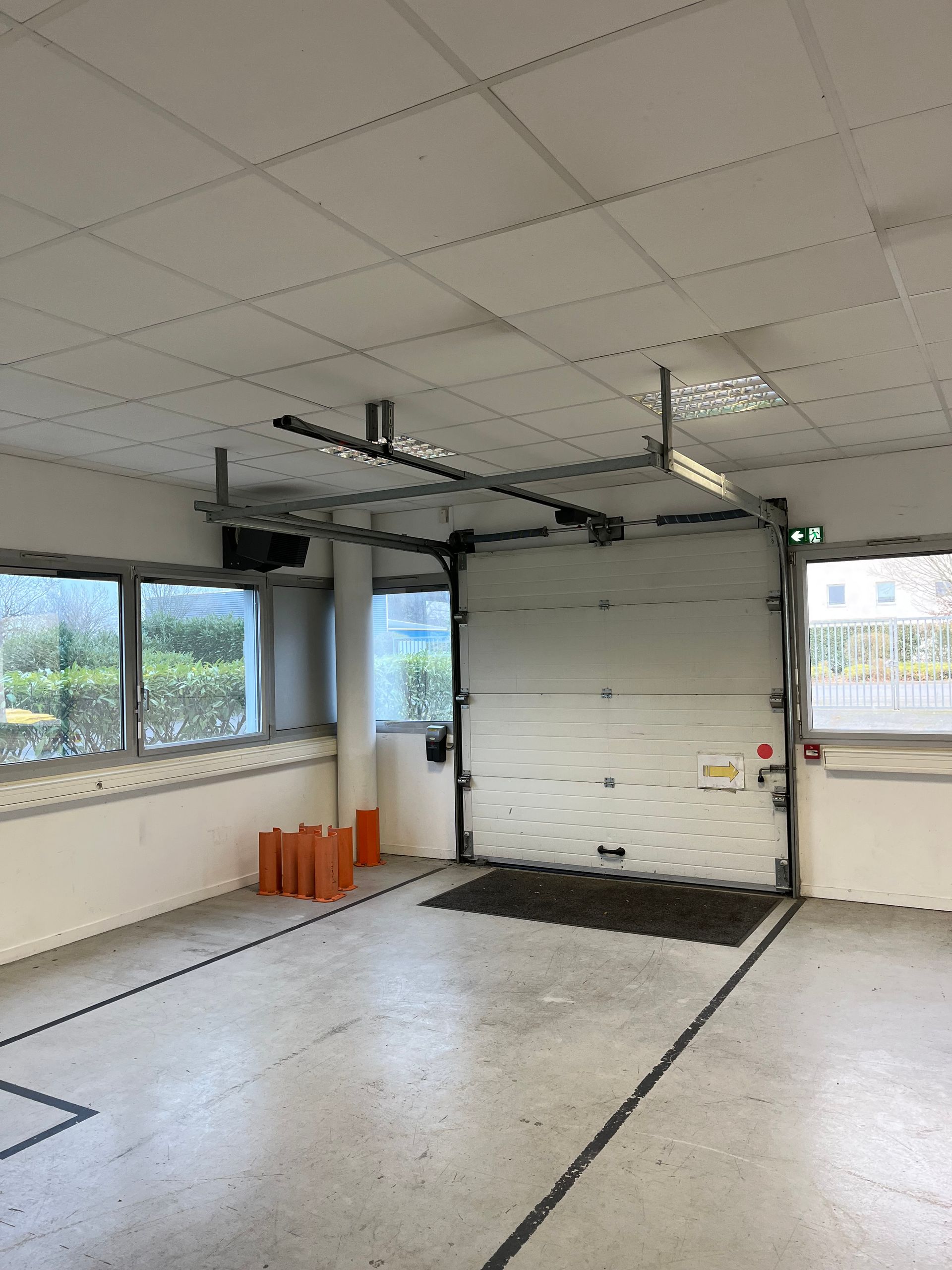 Intérieur du garage avec porte ouverte, fenêtres et mécanisme de plafond. Sol en béton avec lignes peintes.