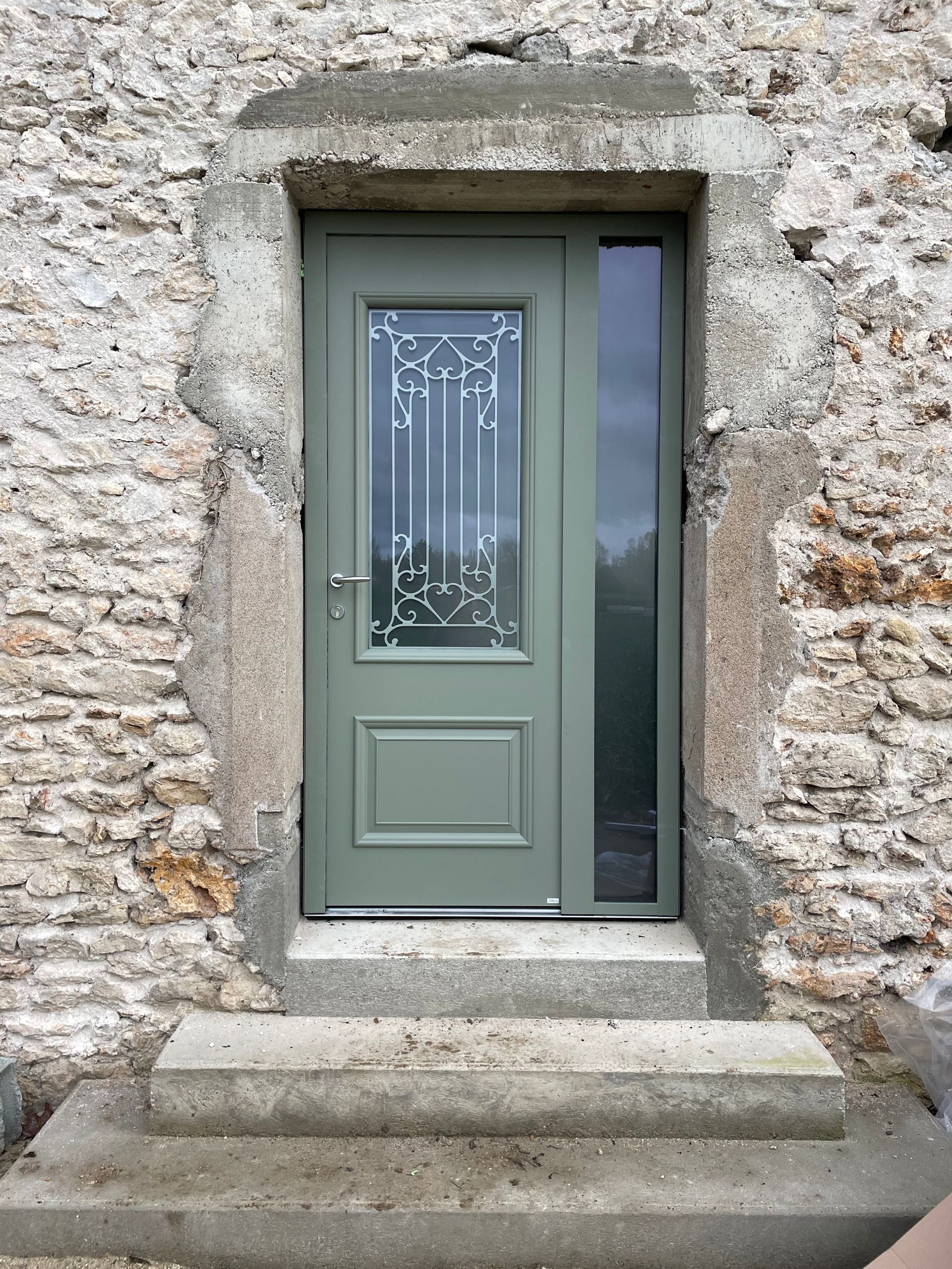 Porte d'entrée grise à panneaux de verre, encastrée dans une arche en pierre.