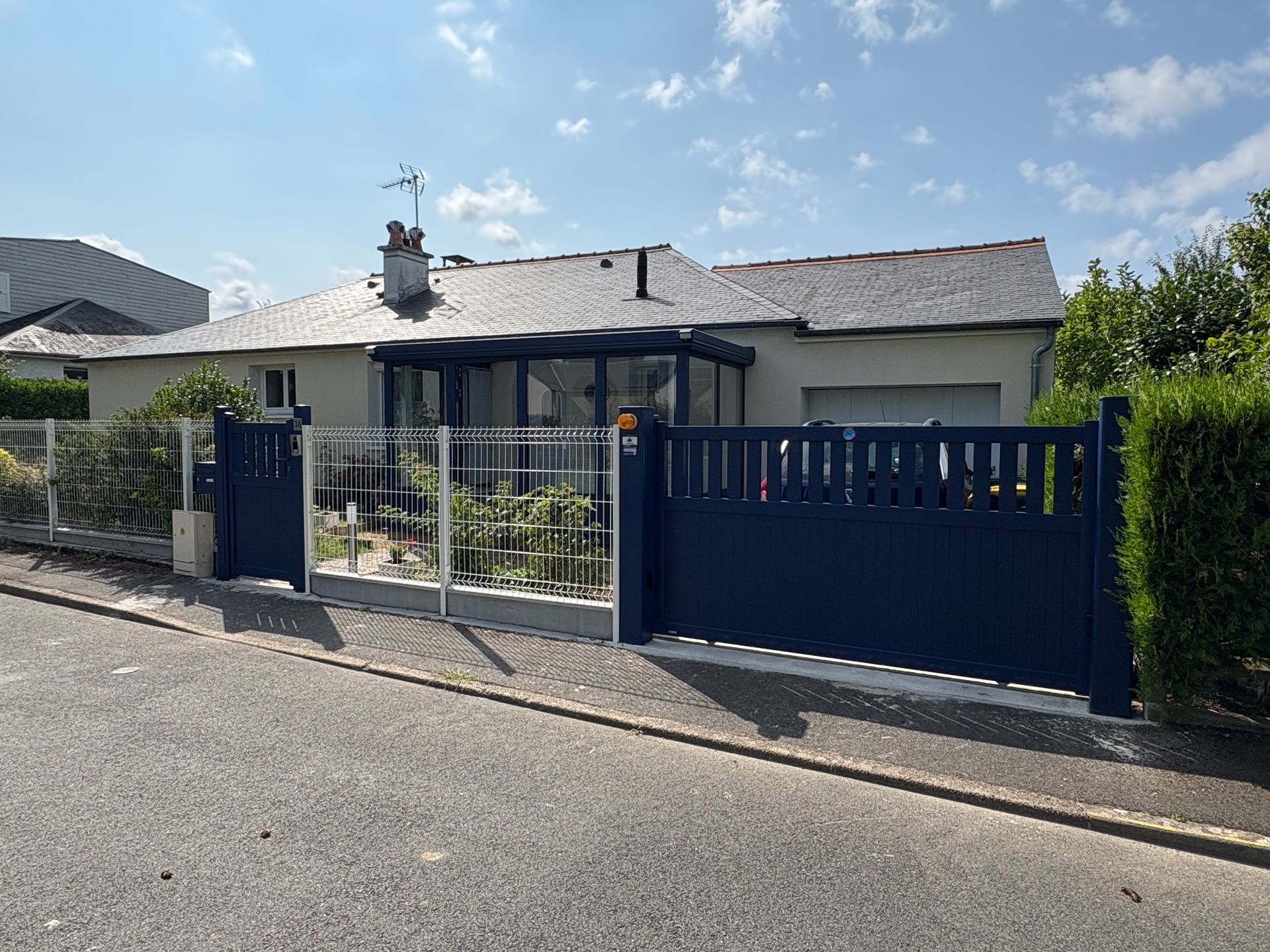 Maison à clôture bleue avec un toit foncé et une véranda vitrée.