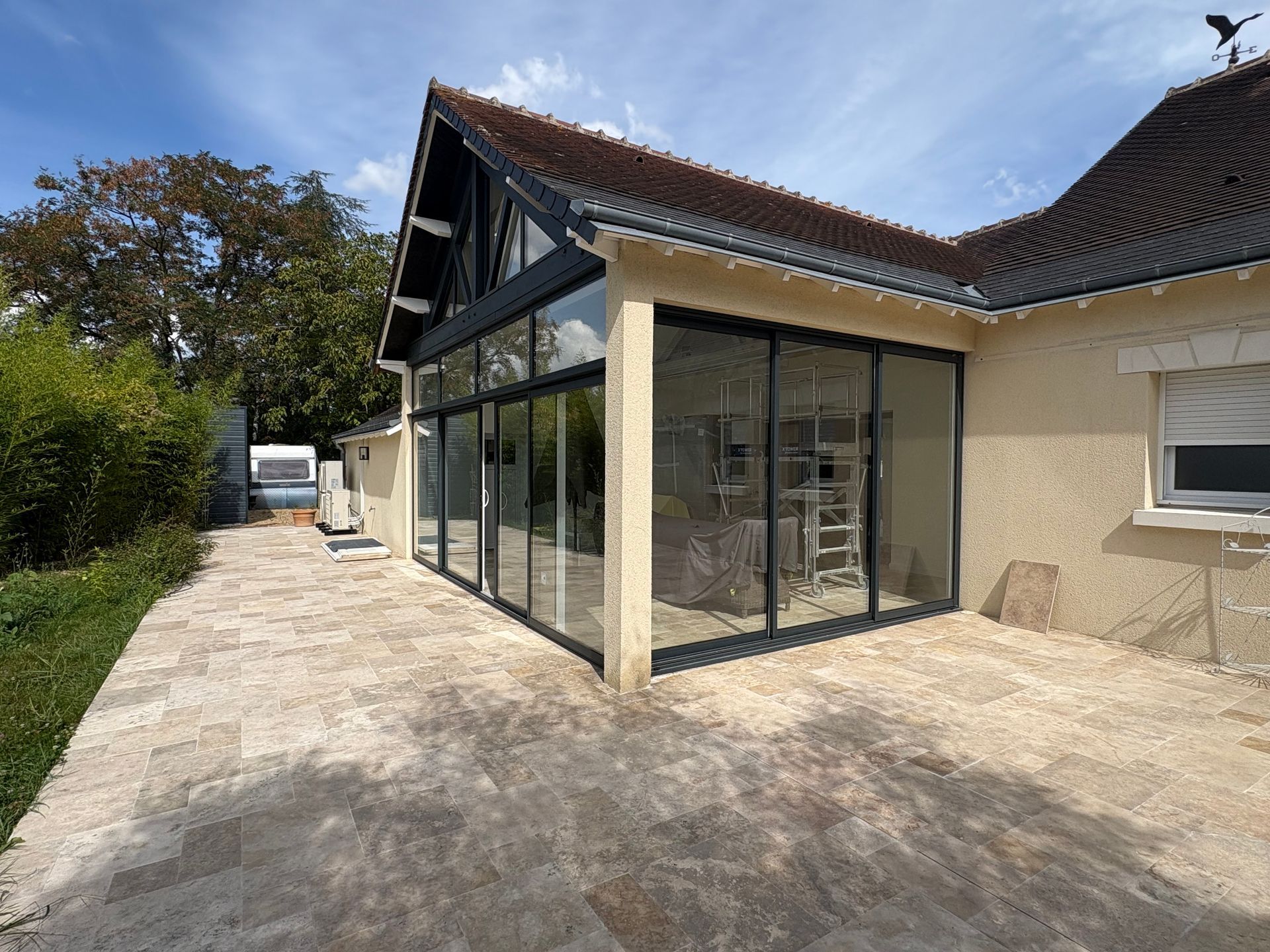 Extension de véranda vitrée avec finitions noires sur une maison beige clair.