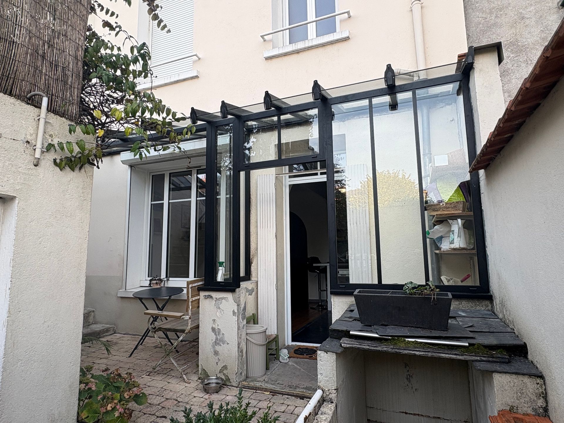 Véranda neuve en aluminium noir contre une petite maison de ville au fond d'une cour.