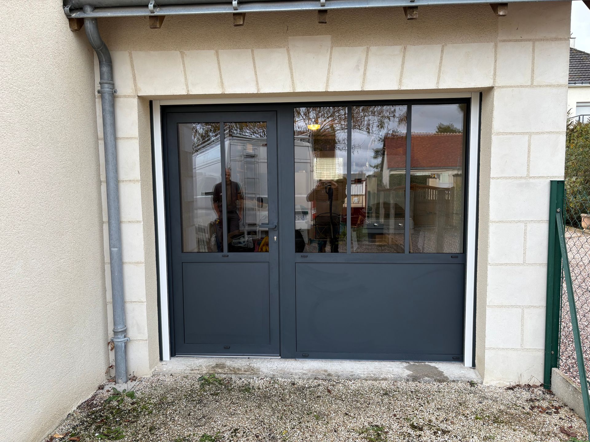 Porte d'entrée grise à panneaux de verre, encastrée dans une arche en pierre.