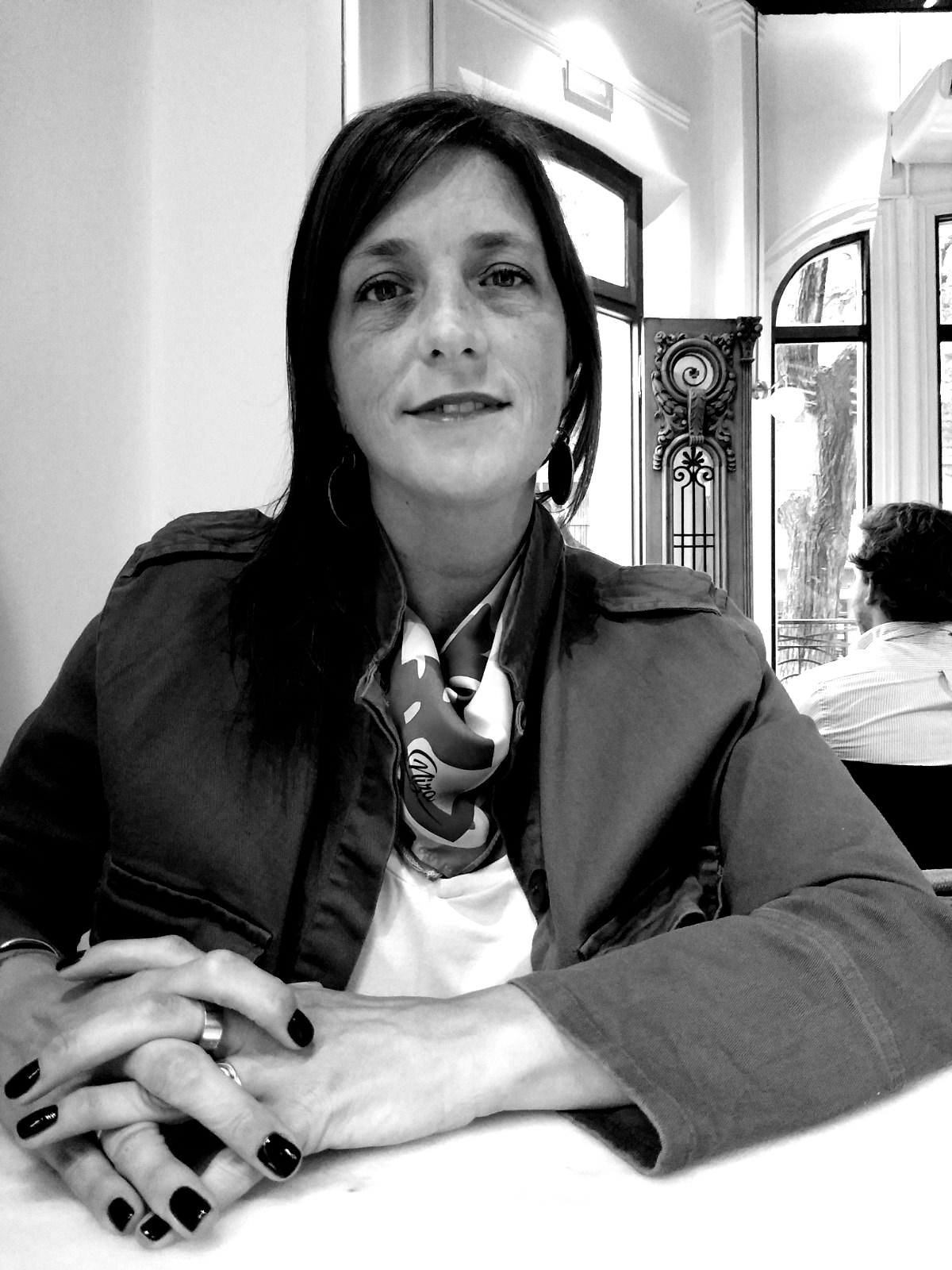 Mujer con cabello largo y oscuro, vestida con un suéter negro, mirando al espectador; manos entrelazadas.
