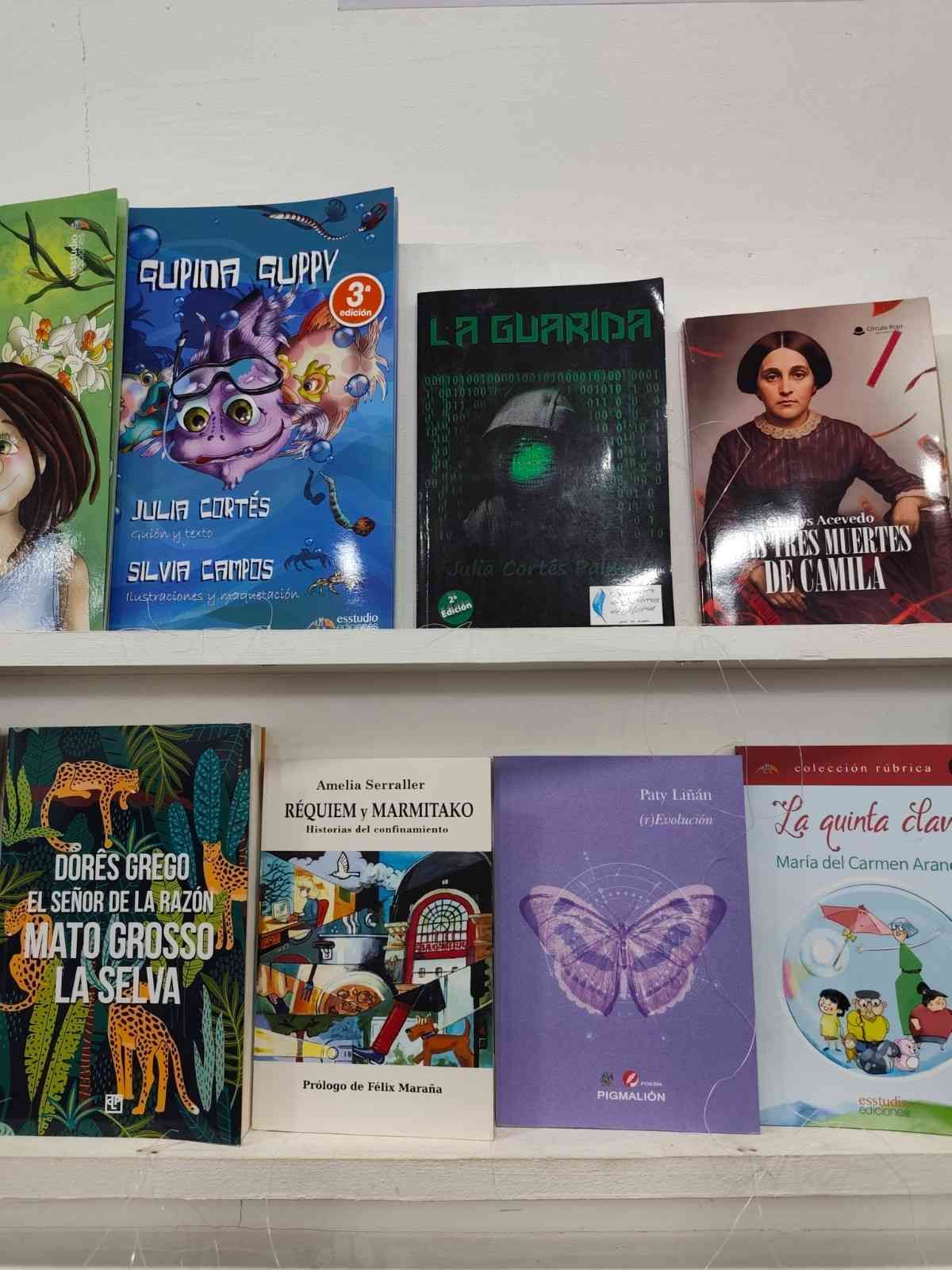 Libros en un estante, varias cubiertas con ilustraciones y texto, incluida una mariposa violeta y escenas de bosques verdes.