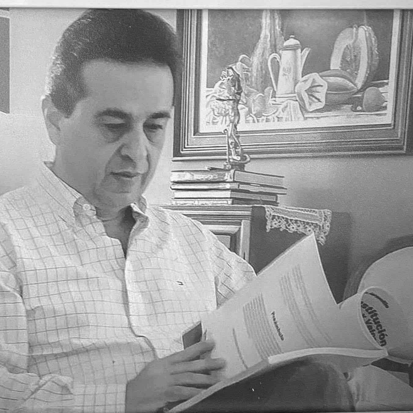 Hombre leyendo un documento en un interior, con un bodegón de fondo.