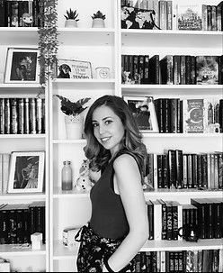 Mujer sonriendo frente a una estantería llena de libros, plantas y decoración.