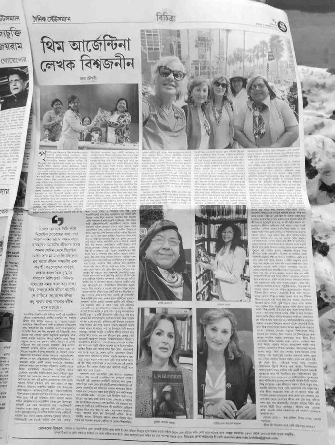 Tres personas hojean libros en un mercado al aire libre: una sostiene una bebida y otra pasa las páginas.