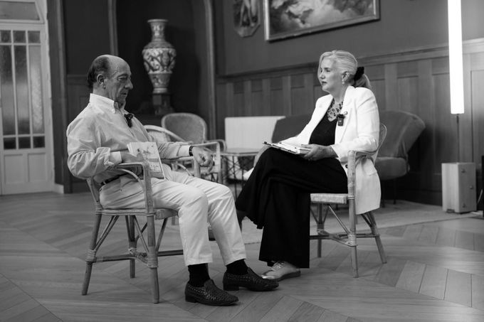 Tres personas hojean libros en un mercado al aire libre: una sostiene una bebida y otra pasa las páginas.