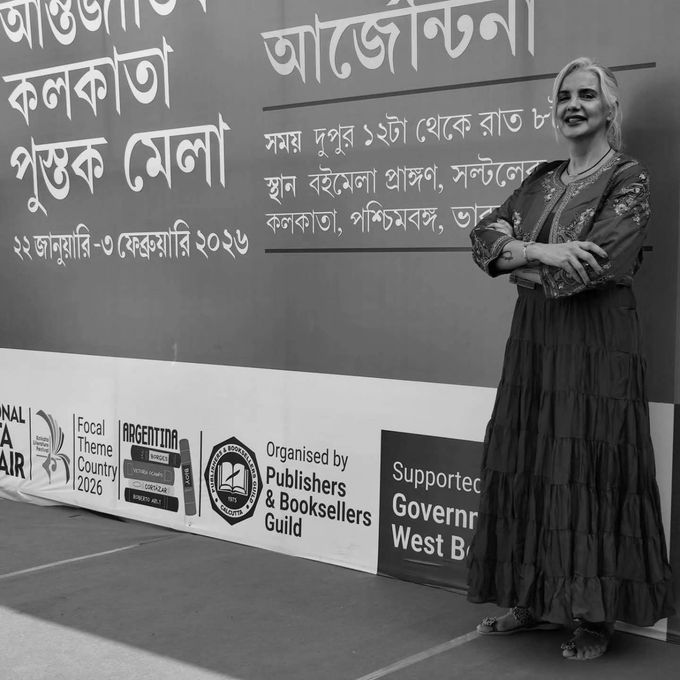 Tres personas hojean libros en un mercado al aire libre: una sostiene una bebida y otra pasa las páginas.