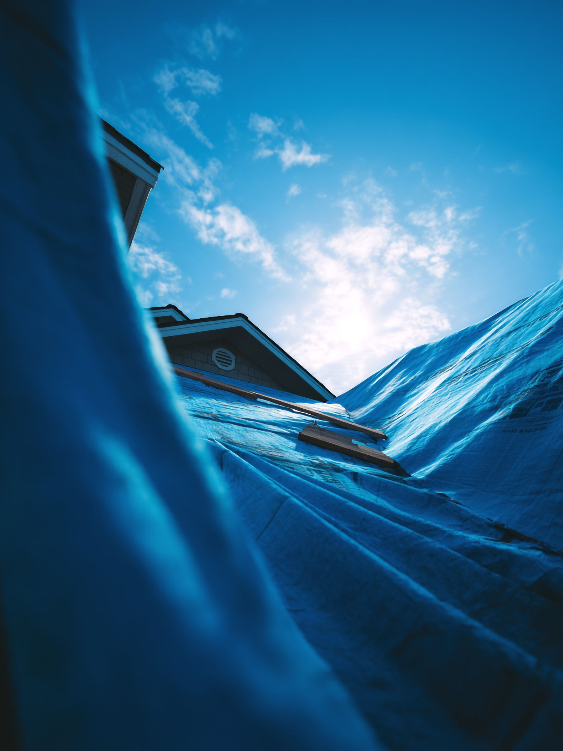 Bâche ou tissu bleu vu d'en bas sur un ciel lumineux, avec le bord d'un bâtiment en arrière-plan.