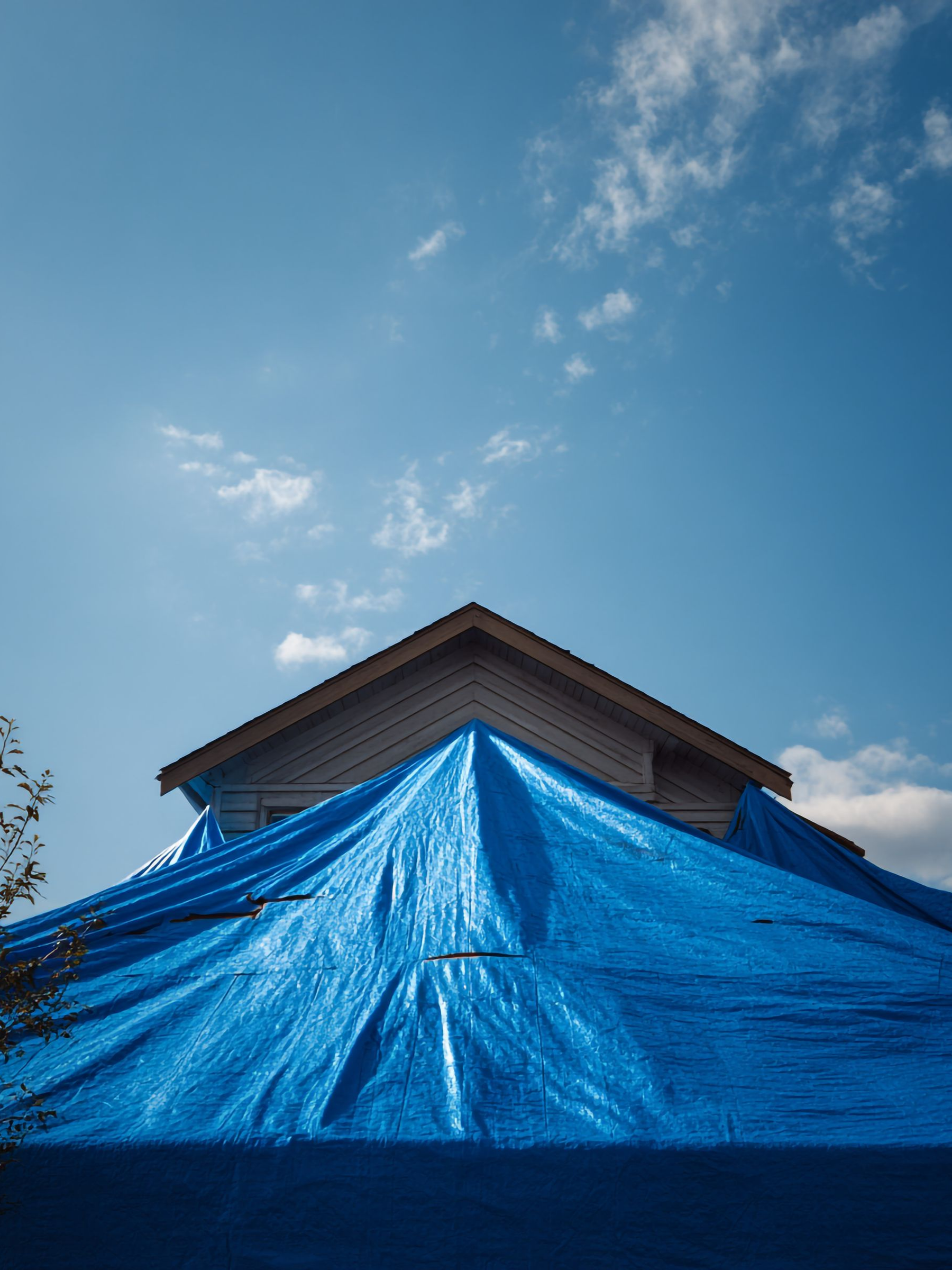 Une bâche bleue recouvre le toit d'une maison sous un ciel bleu clair.