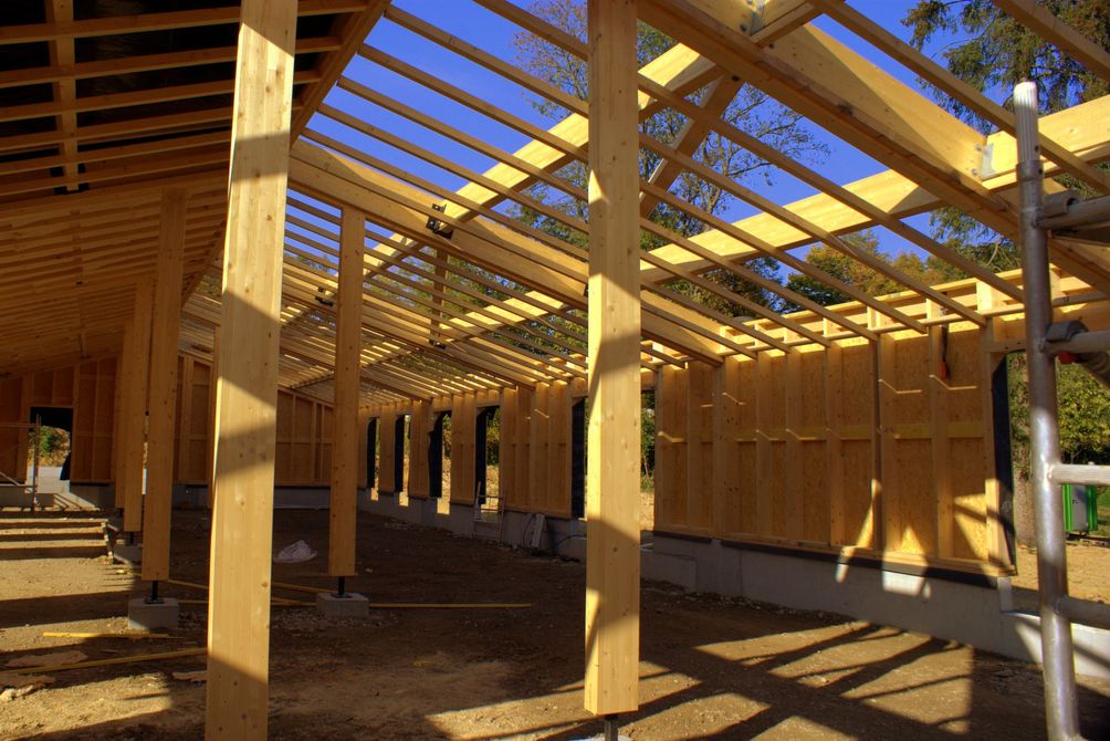 Structure en bois partiellement construite avec poutres apparentes et charpente ouverte baignée de soleil
