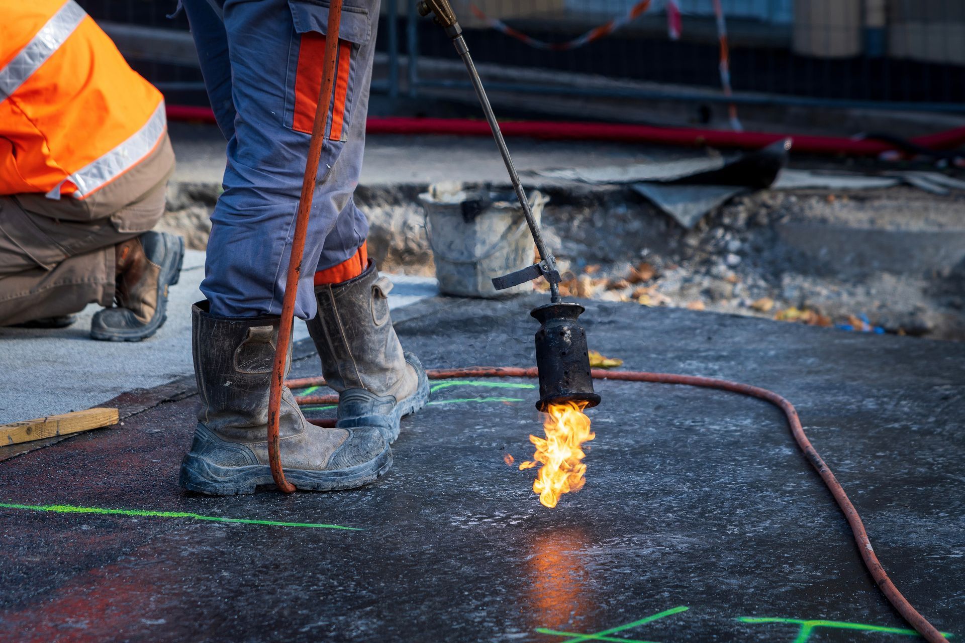 Un ouvrier du bâtiment utilise un chalumeau pour découper la chaussée, provoquant des étincelles sur un chantier routier.