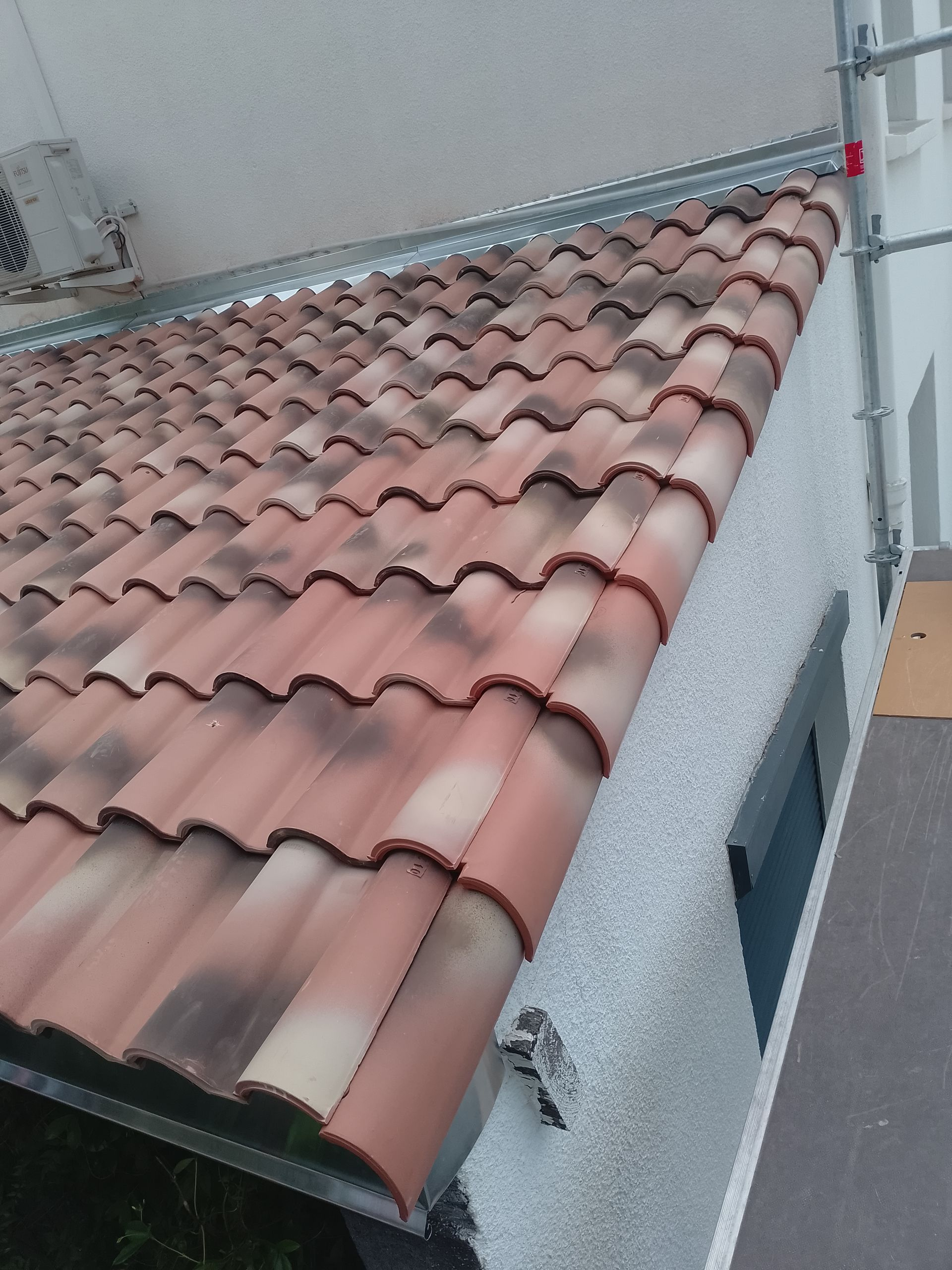 Toit de tuiles rouges sur une maison en stuc gris, vue du ciel nuageux.