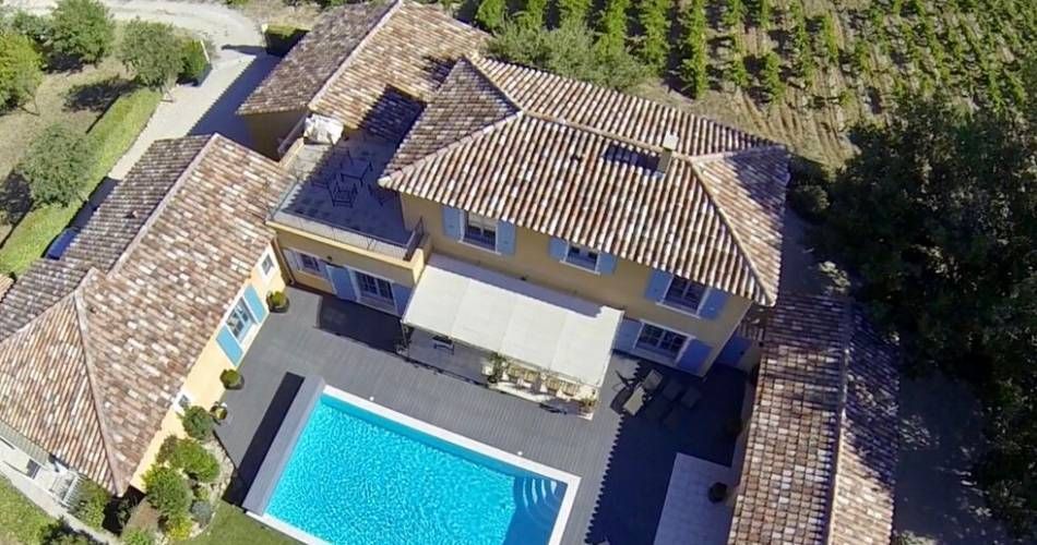 Vue aérienne d'une maison avec un toit de tuiles et une piscine dans le jardin.
