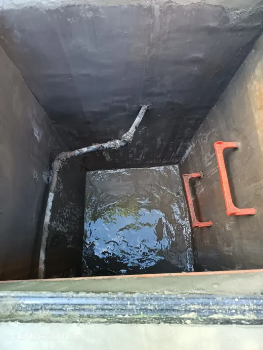 Vista hacia el fondo de un pozo de servicio de hormigón oscuro, con agua en el fondo y manijas metálicas