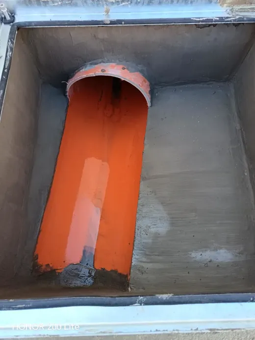 Tubería naranja dentro de una caja metálica gris, con una abertura recortada en la parte superior.