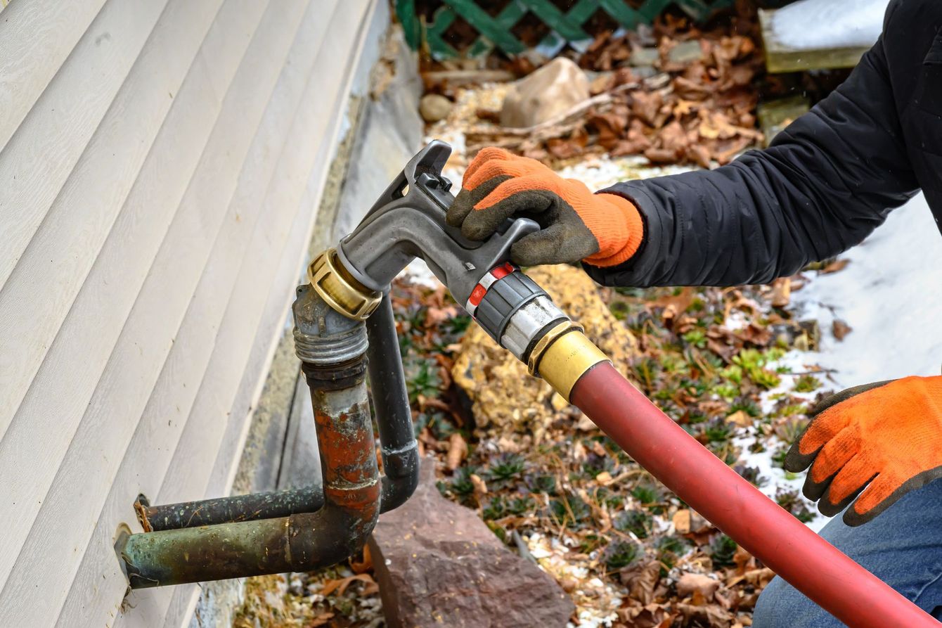 Une personne portant des gants orange manipule une clé à molette sur une conduite d'eau raccordée à un bâtiment. Un tuyau rouge est connecté.