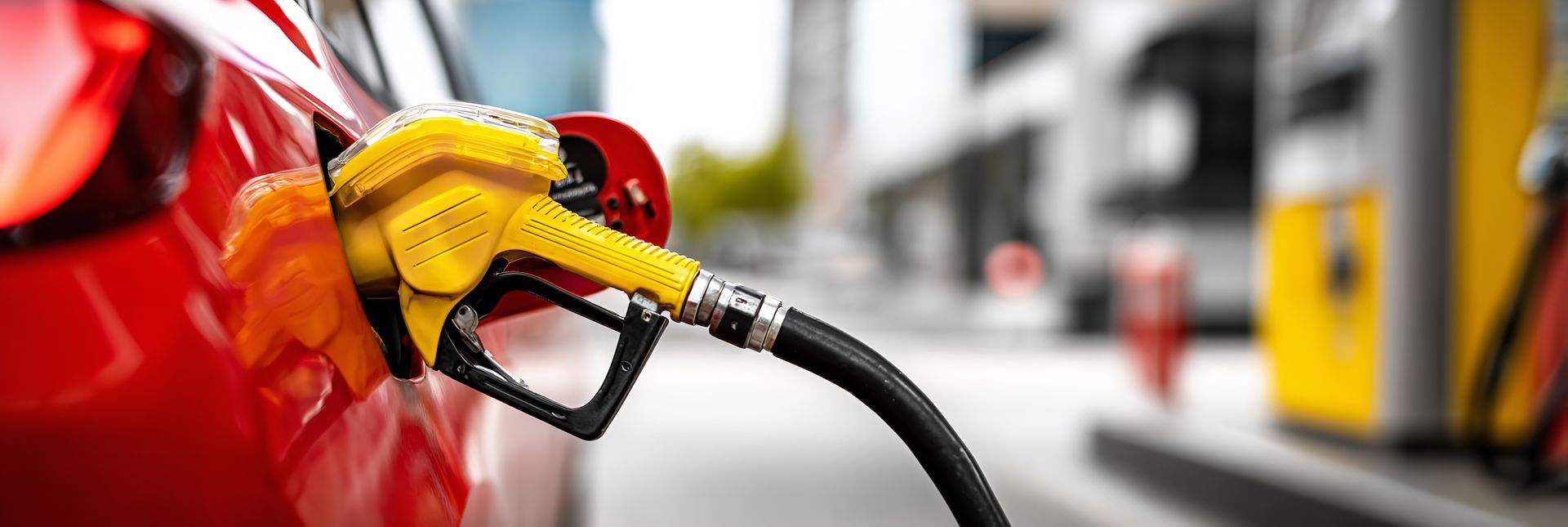 Buse de pompe à essence jaune dans le réservoir de carburant d'une voiture rouge, dans une station-service.