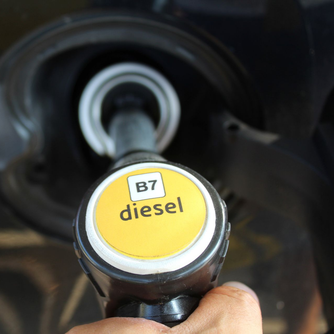 Main tenant une pompe à diesel, remplissant le réservoir d'une voiture. La pompe indique « diesel B7 ».