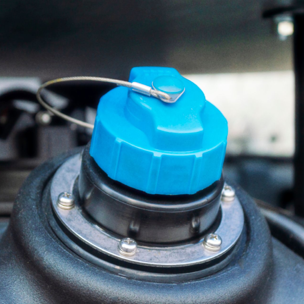 Bouchon de réservoir de liquide d'échappement diesel (DEF) bleu sur un réservoir noir, avec un anneau métallique et un câble de retenue.