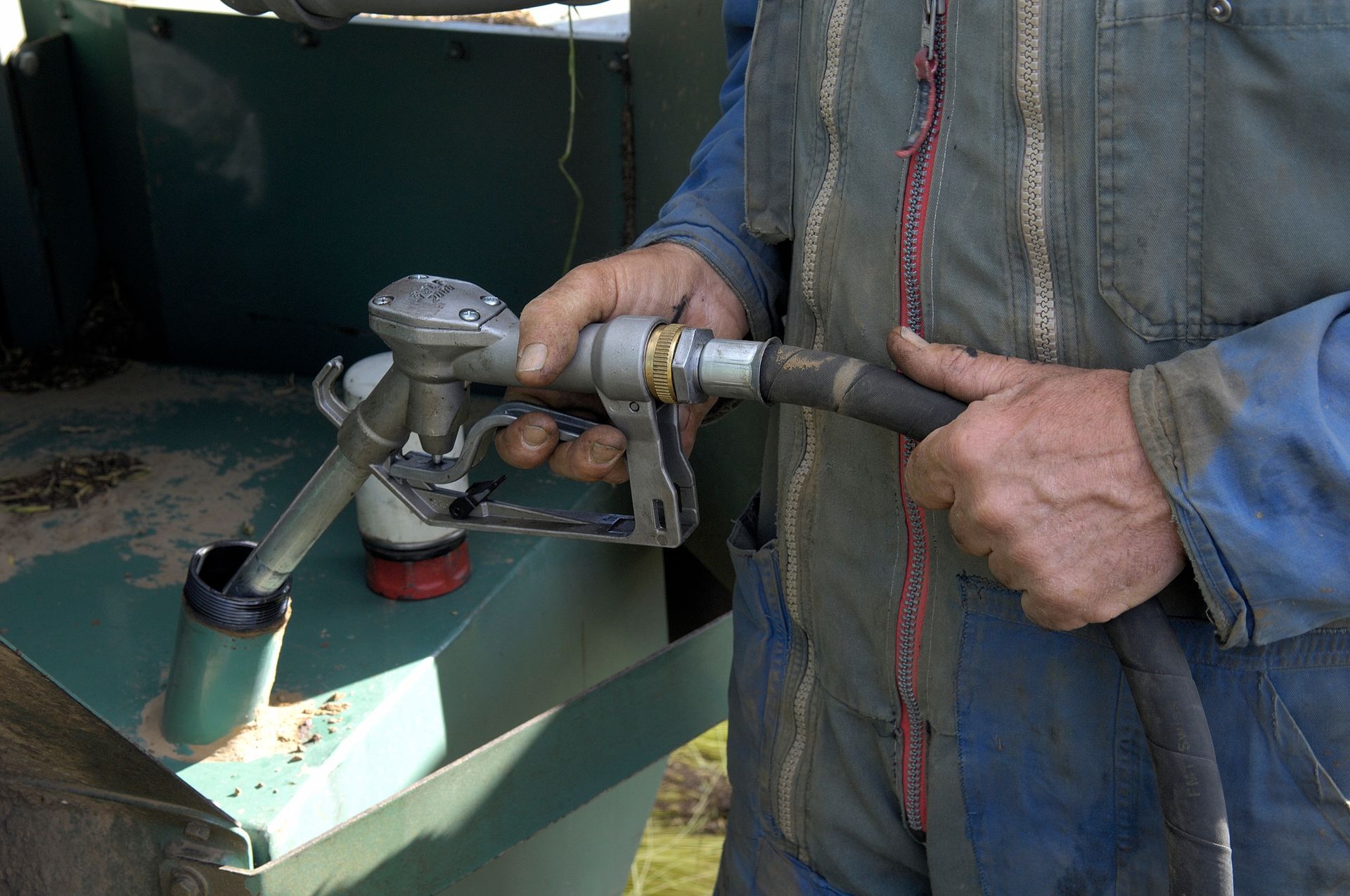 Une personne en salopette bleue fait le plein d'essence avec une pompe à essence.