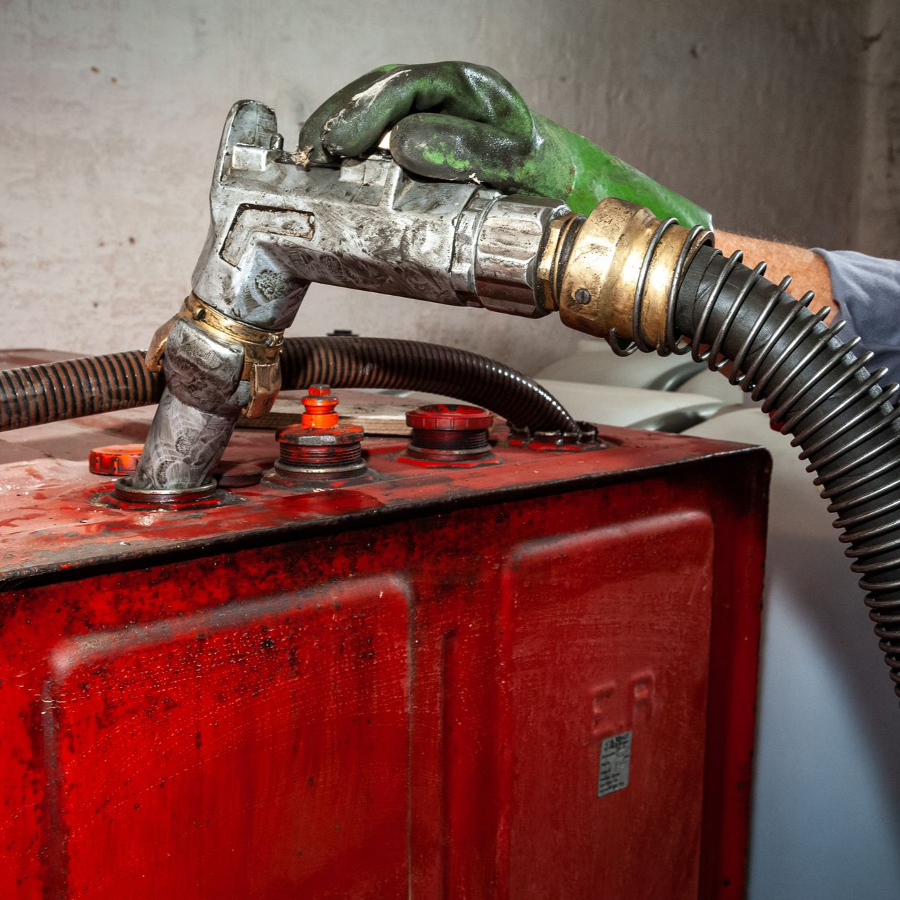 Personne portant un gant vert remplissant un réservoir rouge avec un tuyau.
