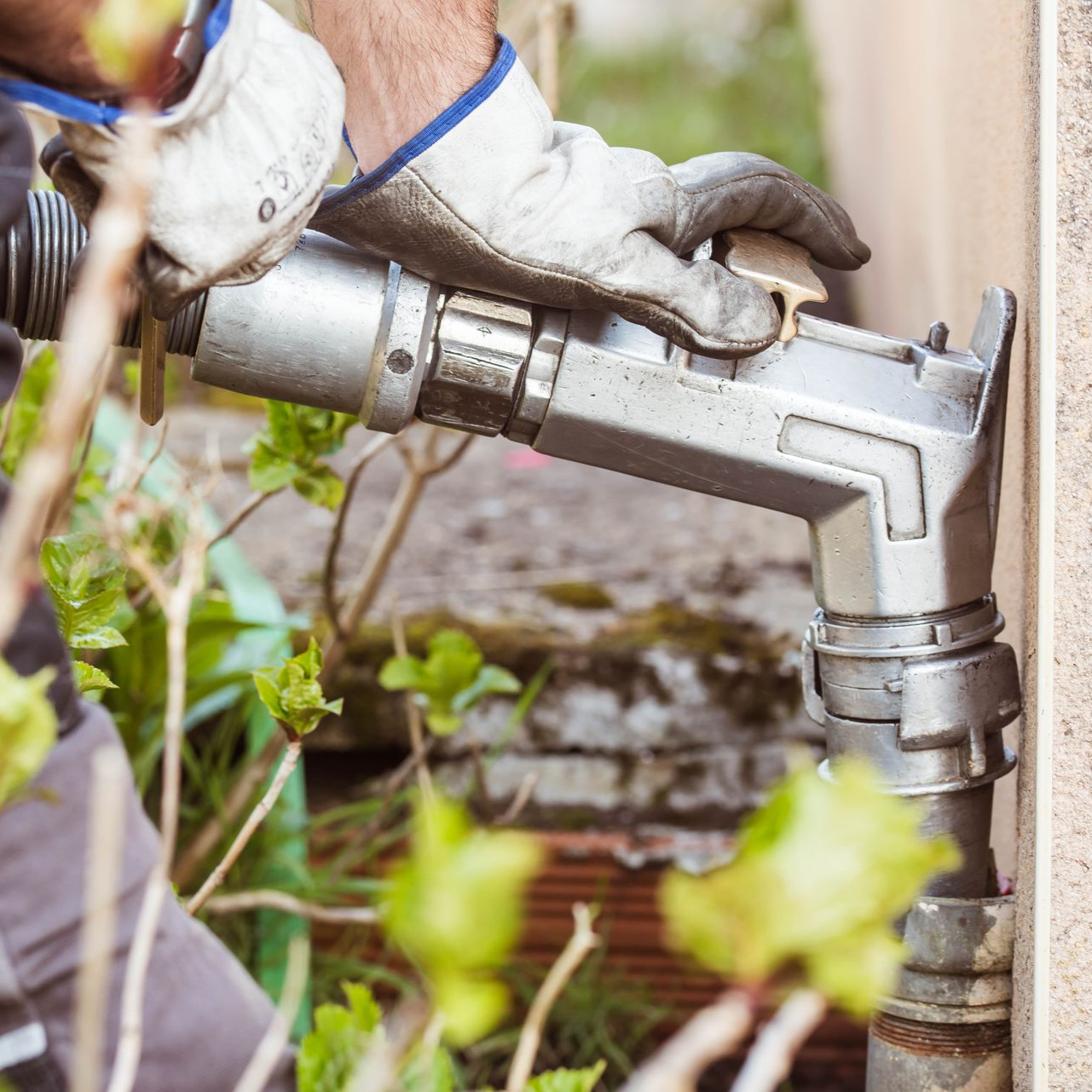 Une personne portant des gants de travail fait le plein d'un réservoir avec un tuyau métallique.