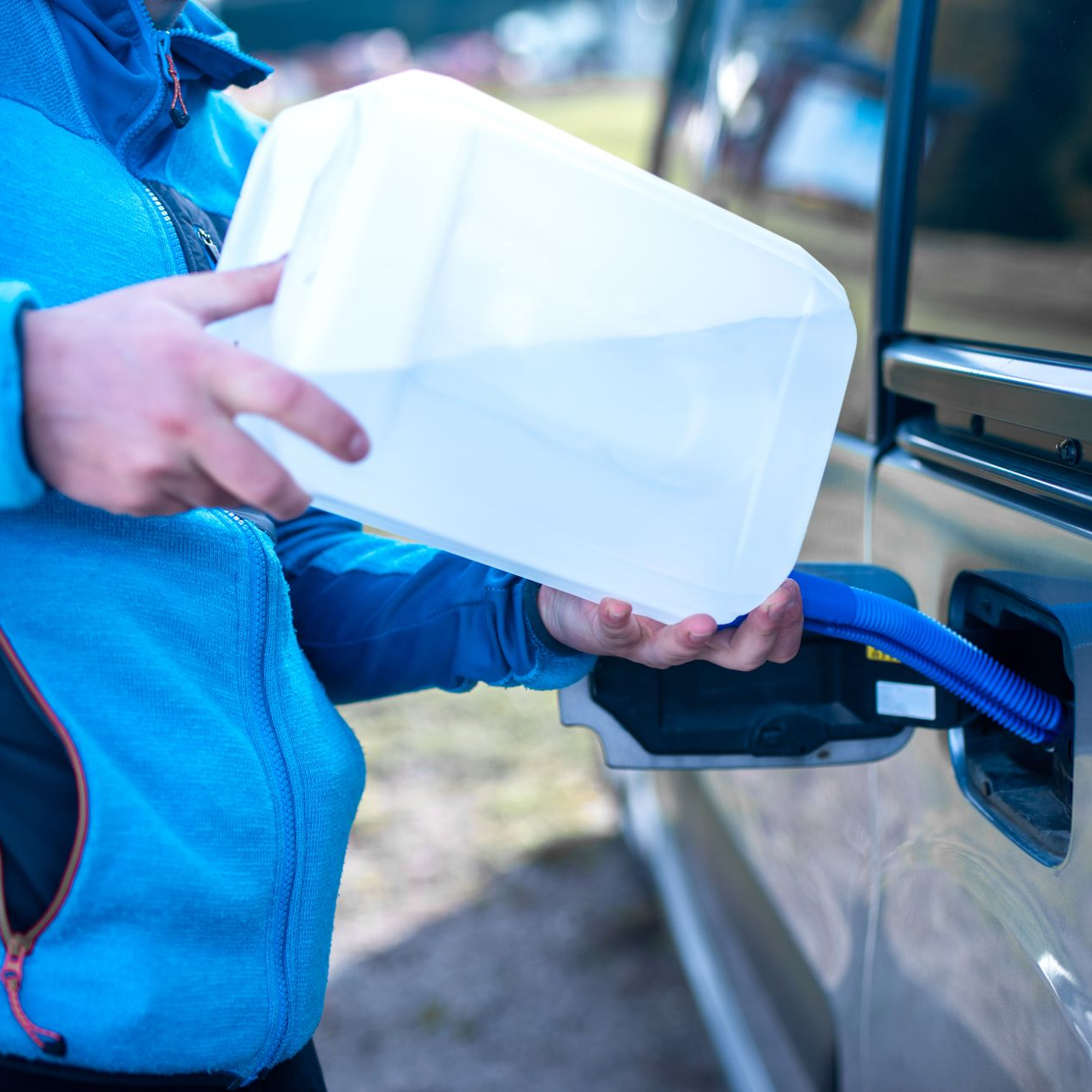 Une personne verse de l'eau d'une cruche dans le réservoir d'essence d'un véhicule.