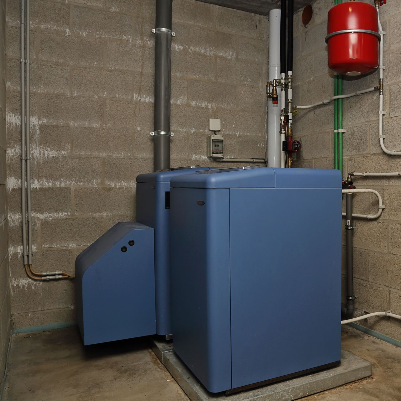 Deux unités de chauffage bleues dans un sous-sol avec des tuyaux et un vase d'expansion rouge.