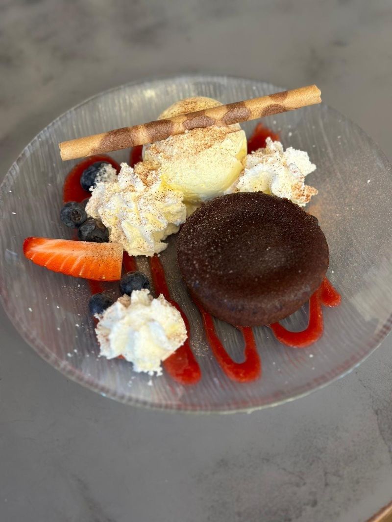 Une assiette de dessert avec de la glace, de la crème fouettée, des fraises et des myrtilles sur une table.