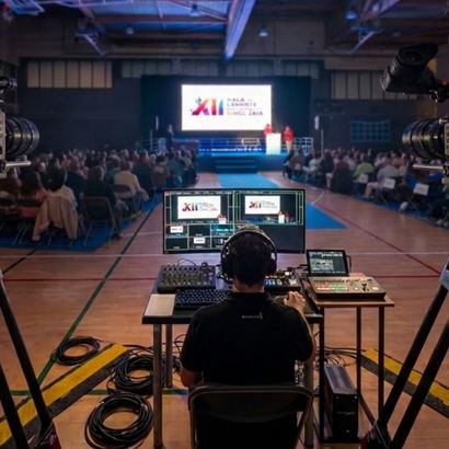 Ingeniero de sonido en una sala de conciertos, controlando el audio desde una cabina de mezclas frente a un gran escenario y al público.