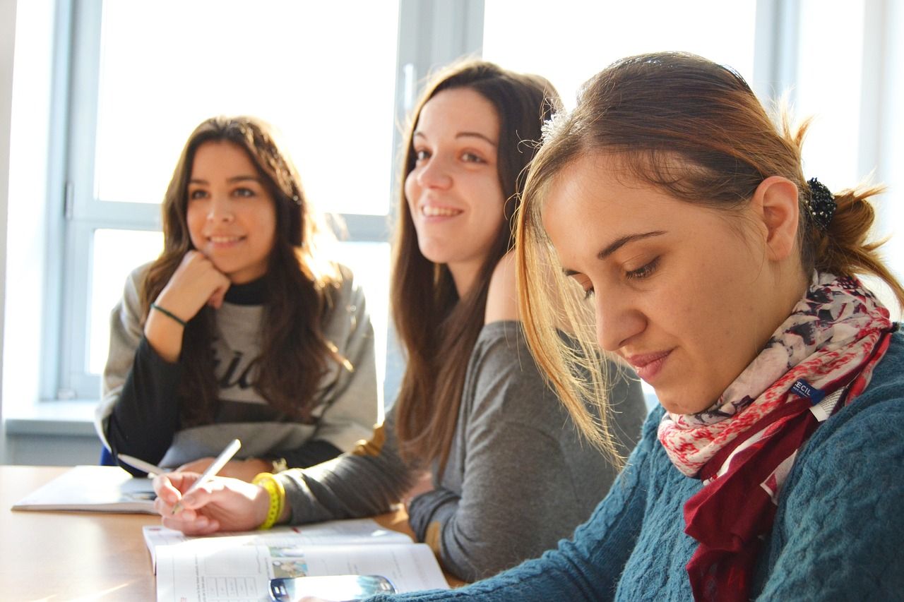 Tres mujeres jóvenes están sentadas en una mesa en un aula.