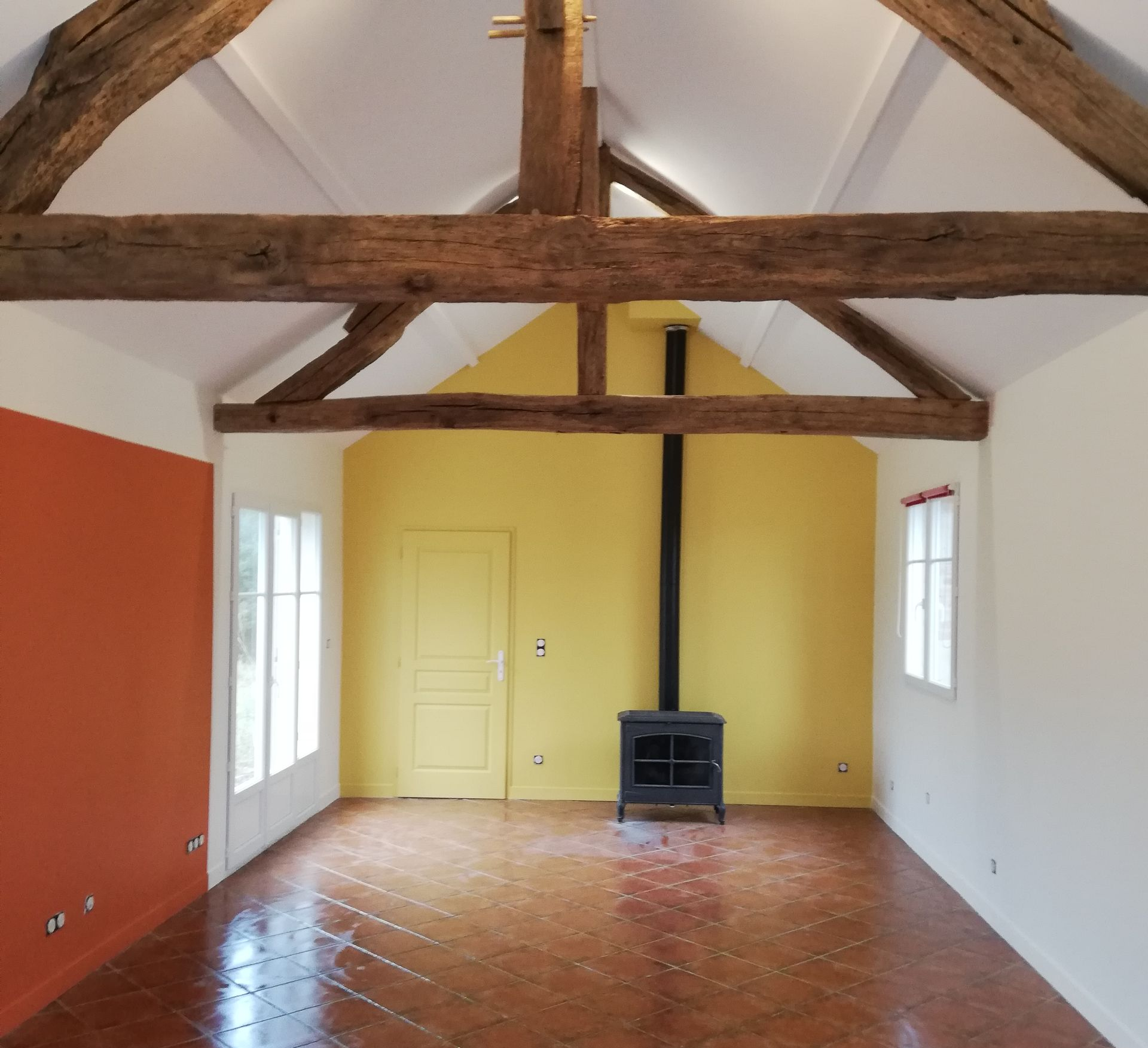 Un salon avec des poutres apparentes, les murs sont repeints en jaune, blanc et orange