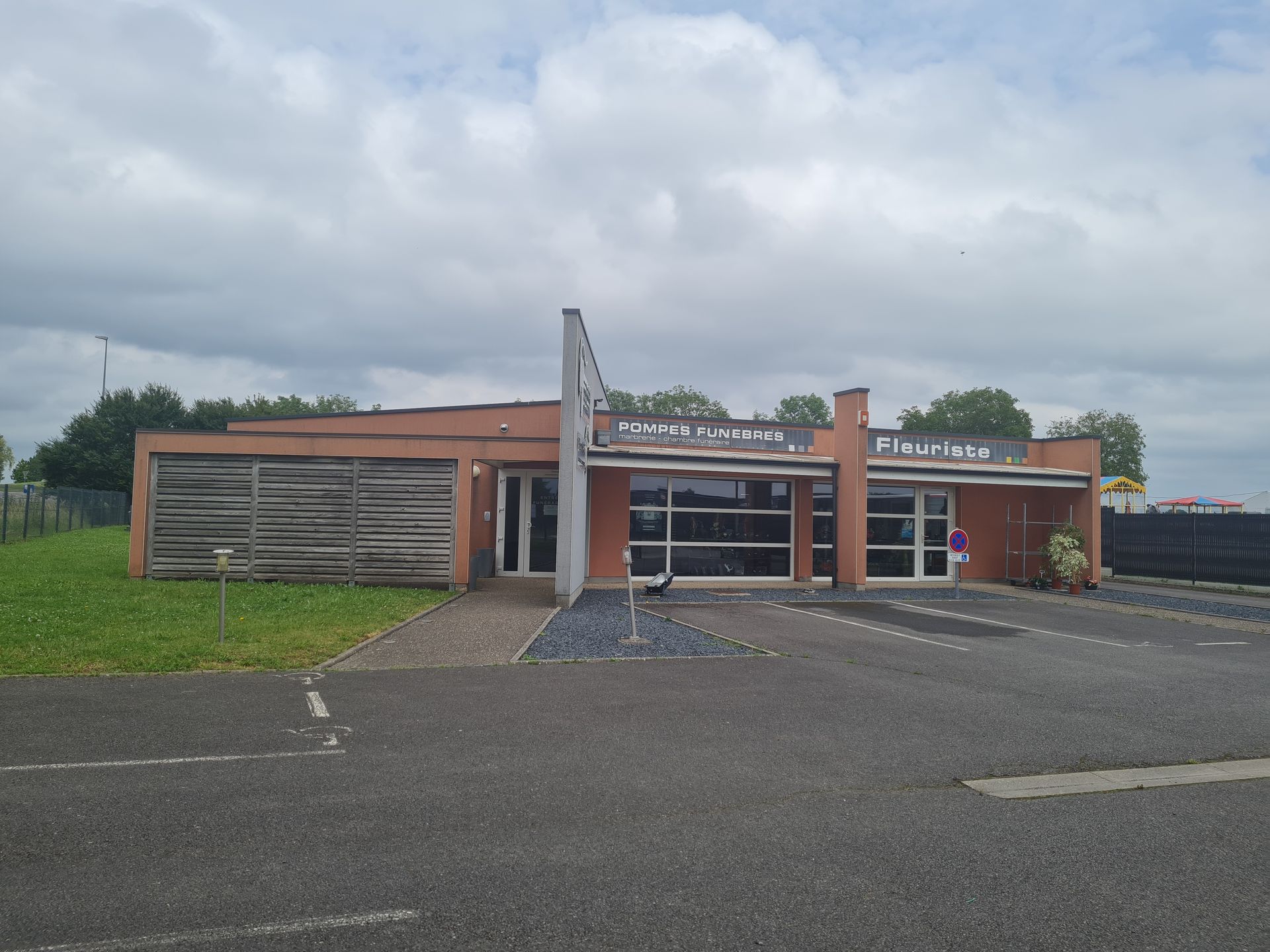 Un bâtiment bas en briques rouges avec de grandes fenêtres et un toit plat, se détachant sur un ciel nuageux.