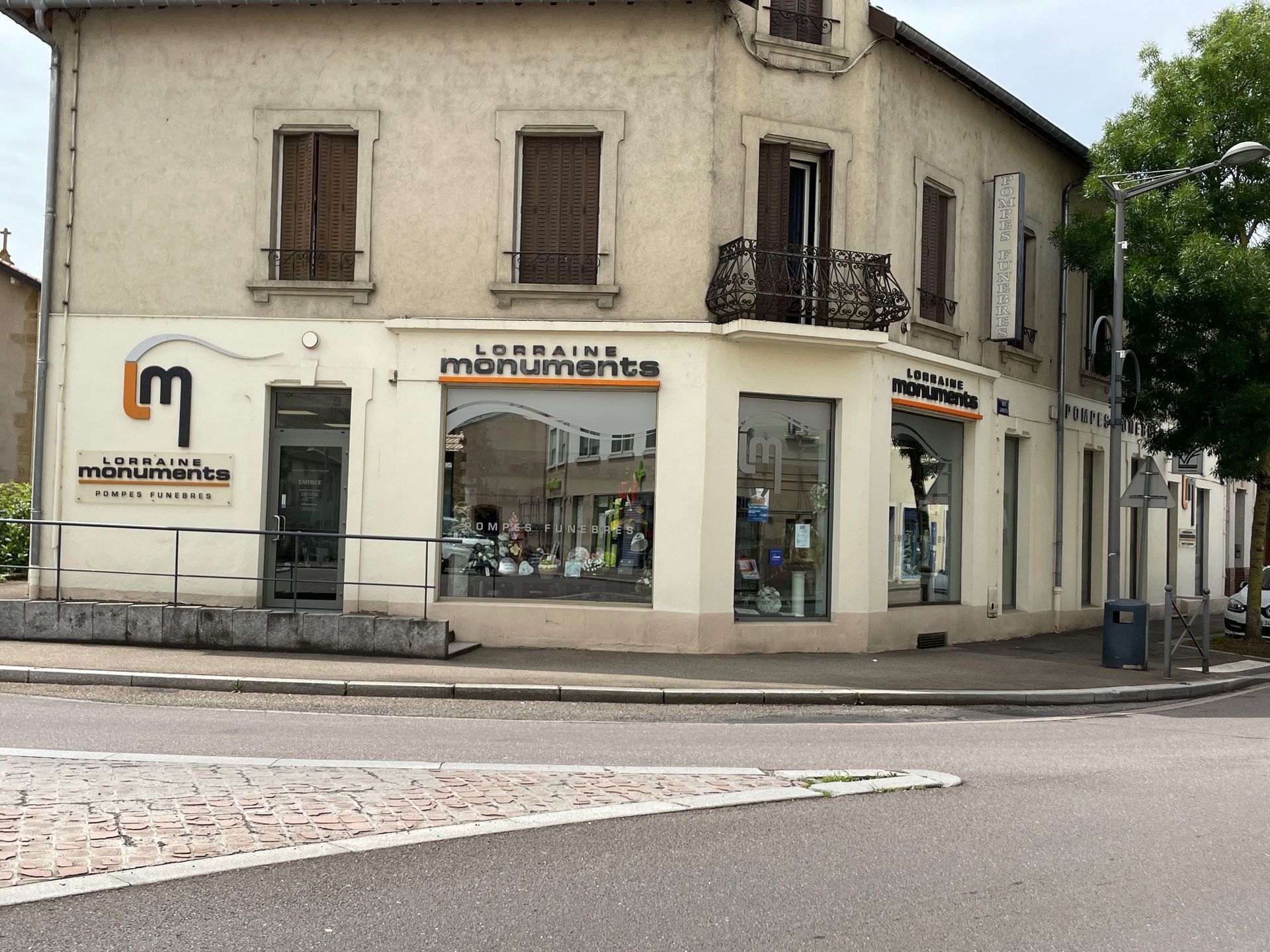 Devanture d'un immeuble d'angle : Monuments lorrains, pierre, vitrine, fenêtres, volets marron. Vue extérieure.