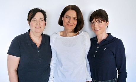 Drei Frauen posieren zusammen für ein Foto und lächeln in die Kamera.