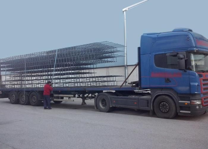 Un hombre está parado al lado de un camión semirremolque azul con un remolque lleno de pilas de metal.