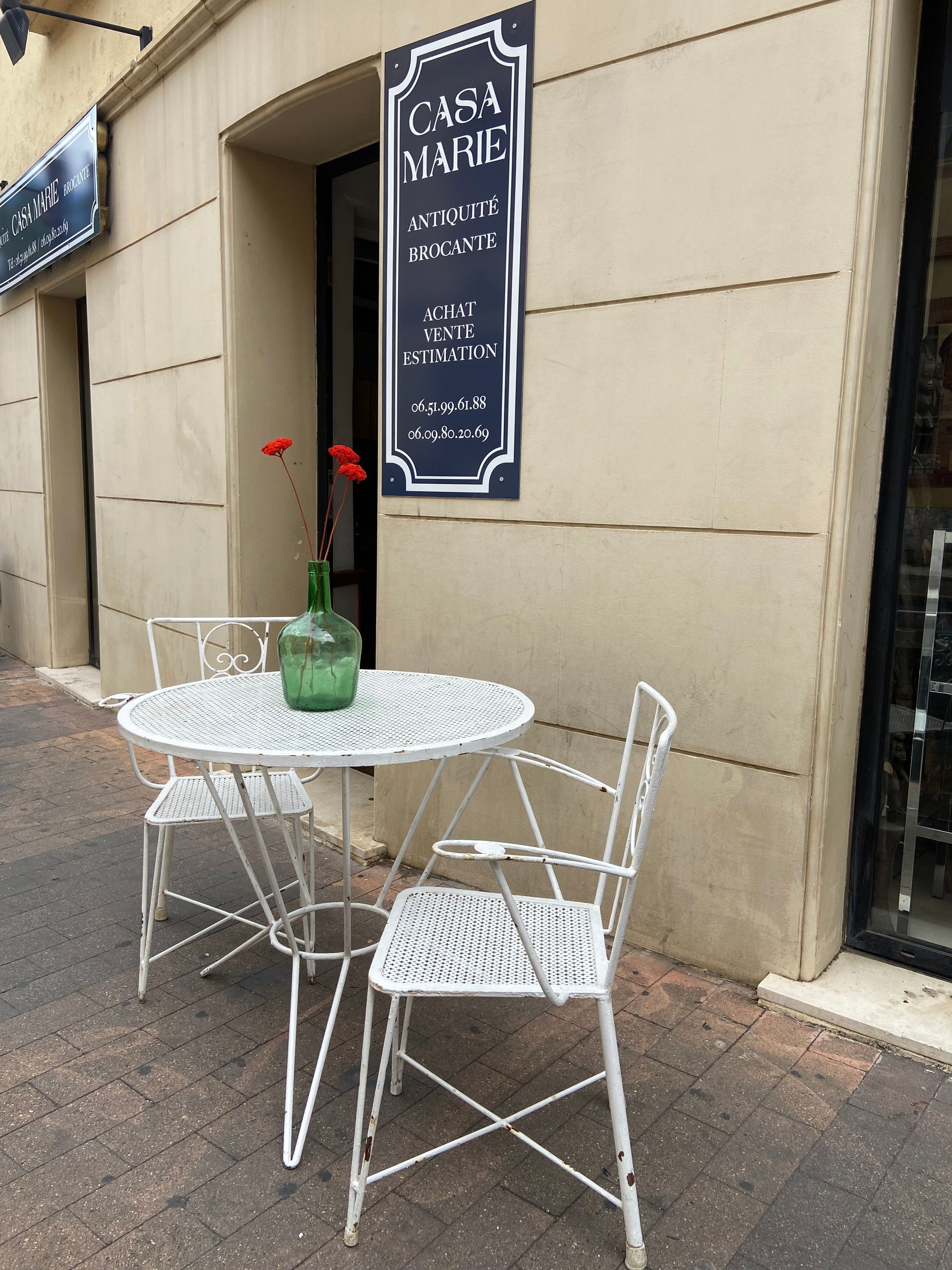Table ronde et chaises blanches en métal avec vase vert contenant trois fleurs rouges