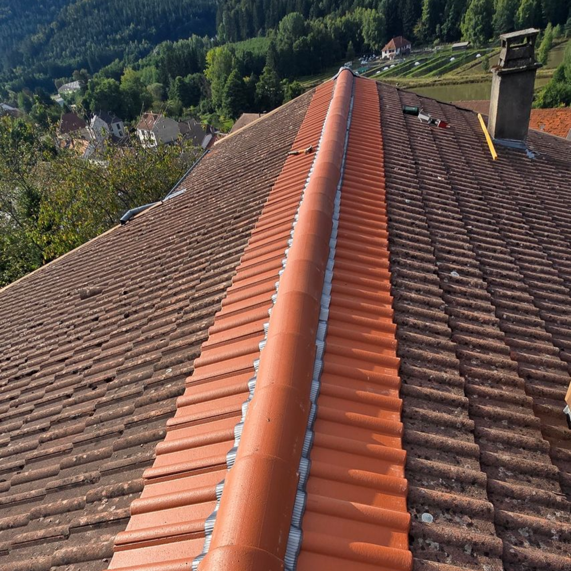 Vue en plongée d'un toit de tuiles présentant une nouvelle faîtière orange recouverte d'un matériau d'étanchéité gris.